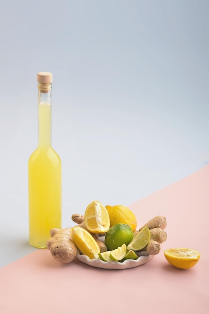 Bottle of homemade juice with ginger and lemon on blue and pink background Vertical