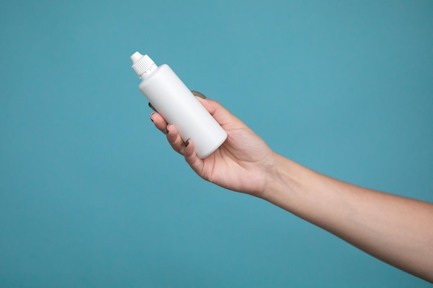 A bottle of liquid for lenses in woman hand on a blue background. Mock up of liquid for lenses