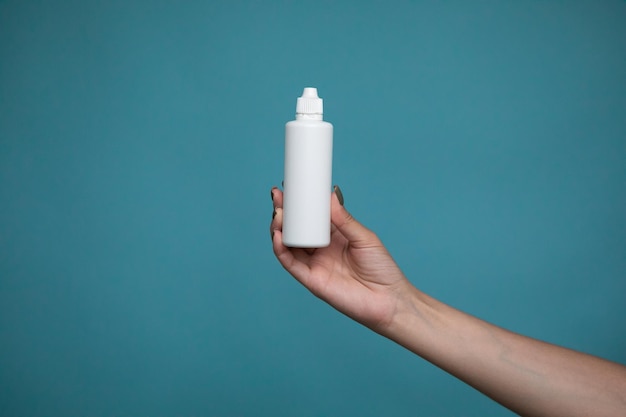 A bottle of liquid for lenses in woman hand on a blue background. Mock up of liquid for lenses