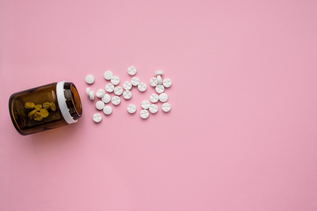 A bottle of medicines and scattered pills on a pastel pink background. Ripped vitamins on a bright background. Flat lay Top view.