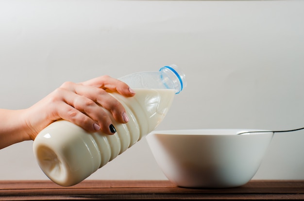 A bottle of milk in a female hand over a white plate. Healthy ea