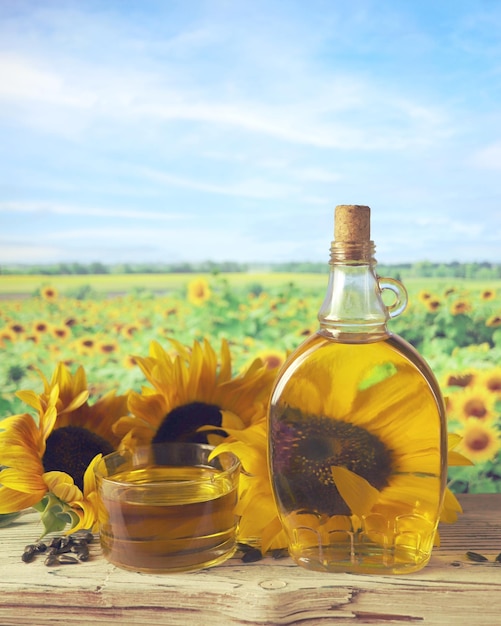 A bottle of oil, fresh sunflower flowers and seeds on the table, a landscape with a flowering field