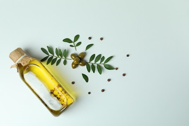 Bottle of oil, olives, twigs and pepper on white surface