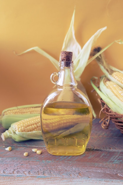 A bottle of oil on the table, against the background of fresh corn with leaves, organic products