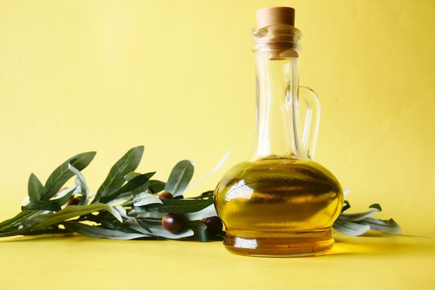 Bottle of olive oil and fresh olive with leaf in a container on yellow