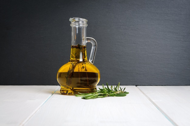 Bottle of olive oil, fresh rosemary branch on white wooden table