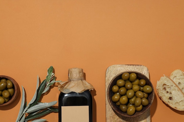 Bottle of olive oil olives in bowls and slices of bread on orange background space for text