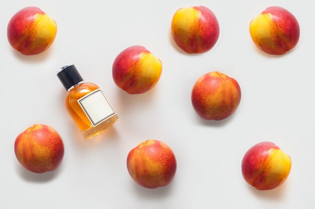 A bottle of peach oil, decorated with a pattern of peaches on a white wall. The concept of an aroma oil, the ingredients of an aroma oil, or aromatherapy.