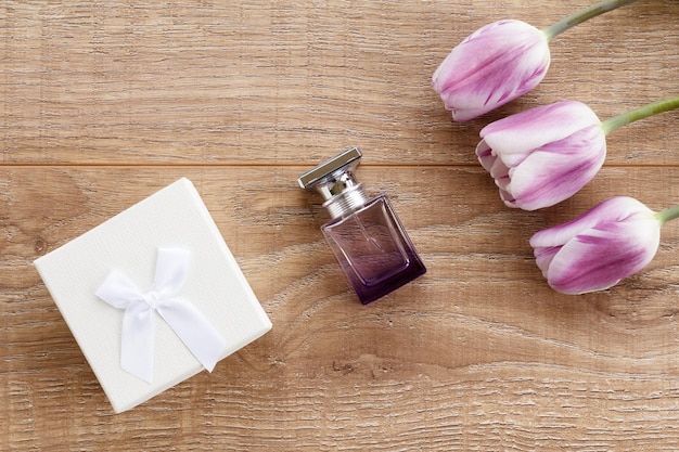 Bottle of perfume and gift box on wooden boards with flowers