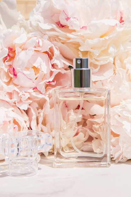 A bottle of perfume made of transparent glass against the background of pink peonies presentation of fragrances advertising of a cosmetic product