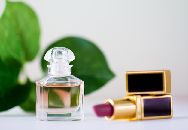 A bottle of perfume and pink lipstick on a of green leaves.