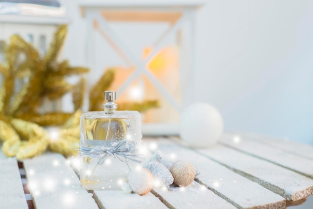 A bottle of perfume tied with a festive ribbon on a snowy wooden surface with balloons with cones ag