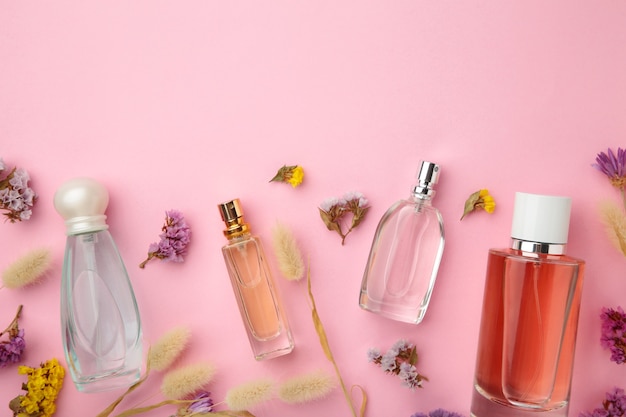 Bottle of perfume with flowers on pink surface with copy space