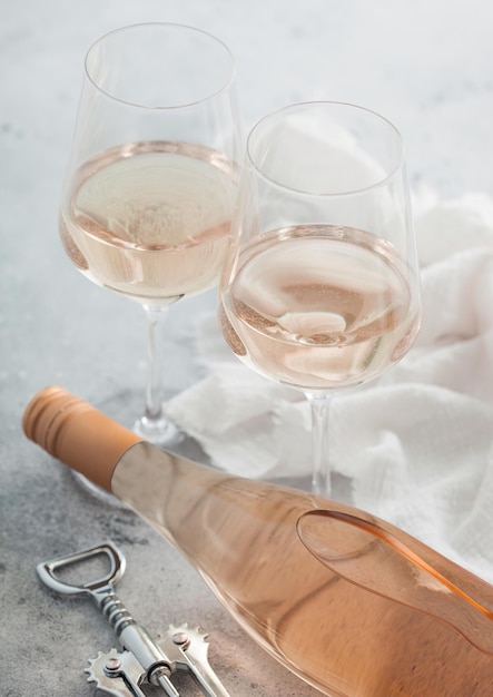 Bottle of pink rose wine with two crystal glasses and steel corkscrew on light table background