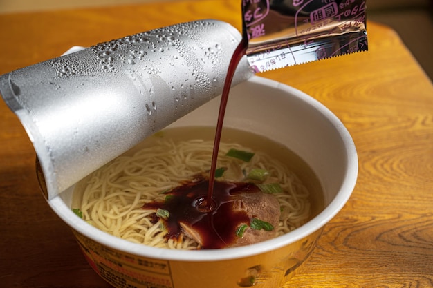 A bottle of ramen is pouring liquid into a cup.