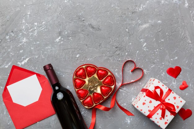 Bottle of red wine on colored background for Valentine Day with gift box envelope and chocolate Heart shaped with gift box of chocolates top view with copy space