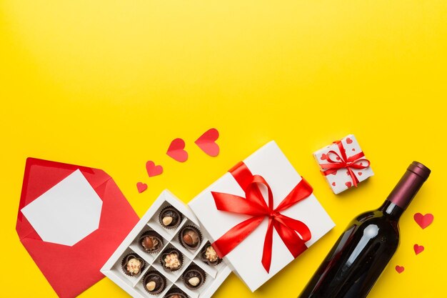 Bottle of red wine on colored background for Valentine Day with gift box envelope and chocolate Heart shaped with gift box of chocolates top view with copy space