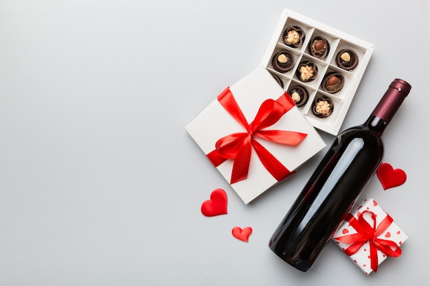 Bottle of red wine on colored background for Valentine Day with gift and chocolate Heart shaped with gift box of chocolates top view with copy space