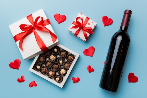 Bottle of red wine on colored background for Valentine Day with gift and chocolate Heart shaped with gift box of chocolates top view with copy space