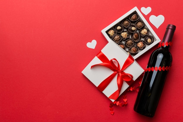 Bottle of red wine on colored background for Valentine Day with gift and chocolate Heart shaped with gift box of chocolates top view with copy space