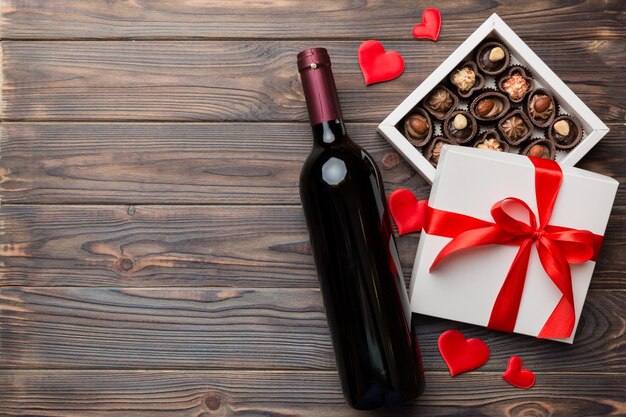 Bottle of red wine on colored background for Valentine Day with gift and chocolate Heart shaped with gift box of chocolates top view with copy space