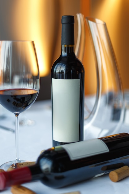 Bottle of red wine, a glass of wine and a decanter on a table with a white tablecloth.