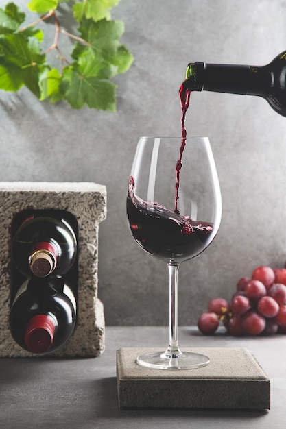 Bottle of red wine poured into the wine glass on concrete background Vertical format Beverage and wine concept