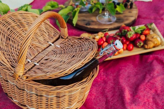 Bottle of red wine in straw basket and plate with berries and croissants near