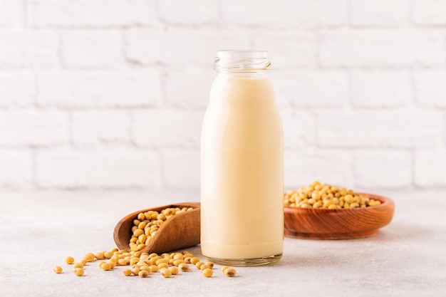 A bottle of soy milk and soy beans on a light background.