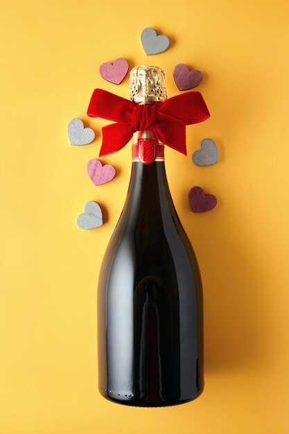 Bottle of sparkling wine tied with ribbon and wooden hearts on a yellow background Festive New Year background