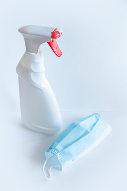 The bottle spray of white color with the red button a liquid soap and medical mask is on a table