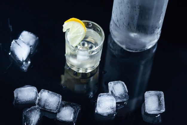 Bottle of vodka and glass with lemon on dark background