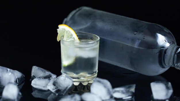 Bottle of vodka and glass with lemon on dark background