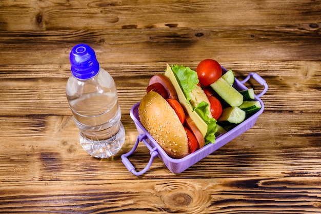 Bottle of water and lunch box with hamburger cucumbers and tomatoes on wooden table