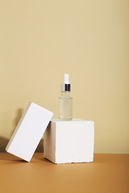 Bottle white glass with dropper on beige background and white box. Natural cosmetic product for skincare concept