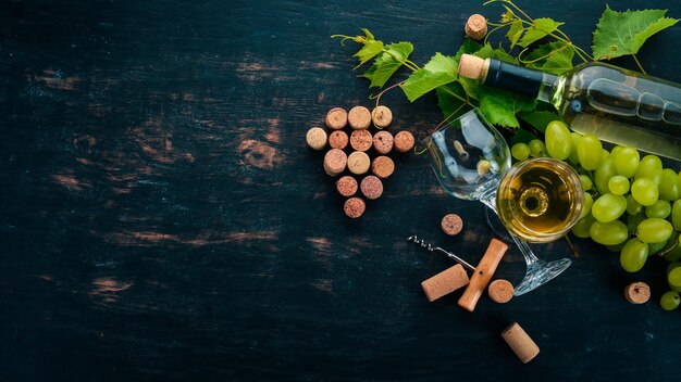 A bottle of white wine with glasses and grapes Leaves of grapes Top view On a black wooden background Free space for text