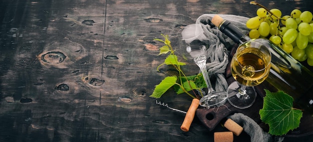 A bottle of white wine with glasses and grapes Leaves of grapes Top view On a black wooden background Free space for text