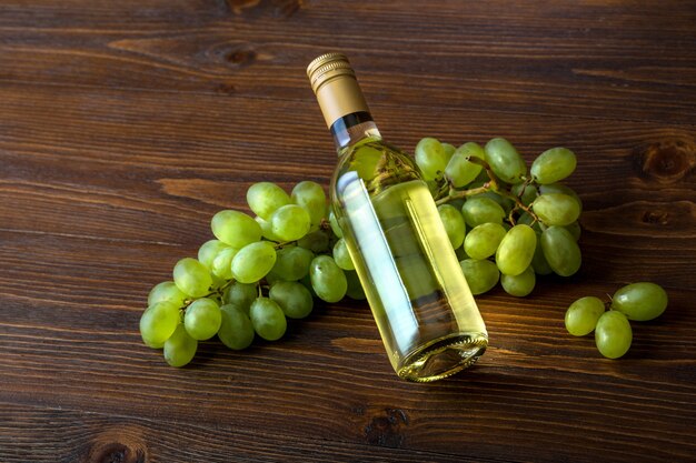 A bottle of white wine with grapes on a wooden background