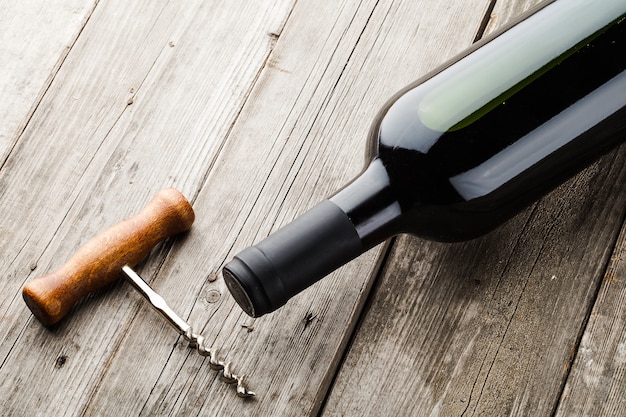 Bottle of wine and corkscrew on wooden backgroumd