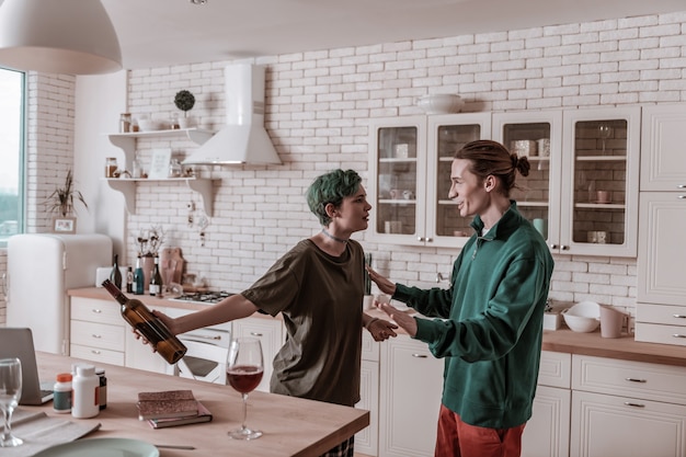 Bottle of wine. Green-haired wife addicted to alcohol holding bottle of wine after drinking on her own