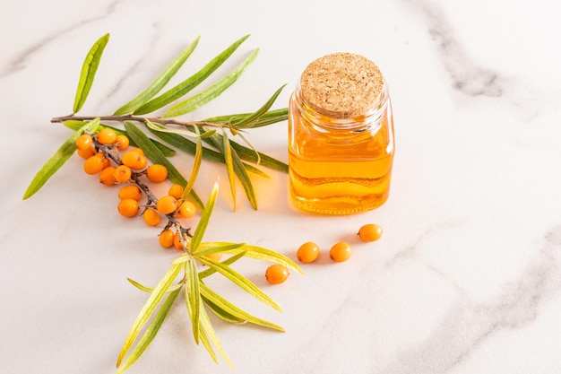 A bottle with a cork with organic natural sea buckthorn oil on a marble background and berries natural elixir of youth and health