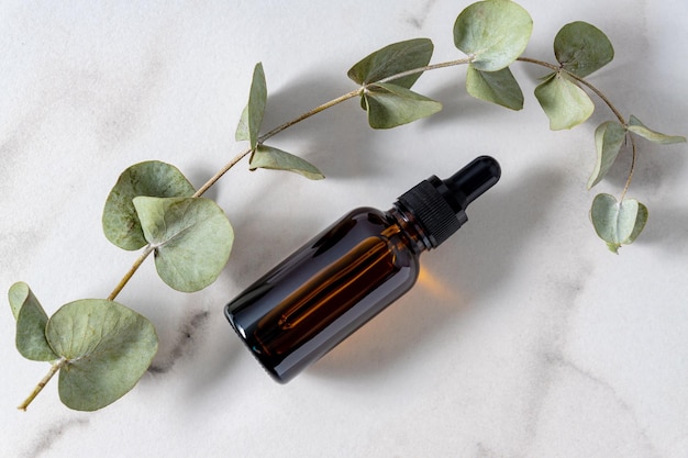 Bottle with essential oil and eucalyptus branches on marble baclground Skin care and healthy treatment for the face and body