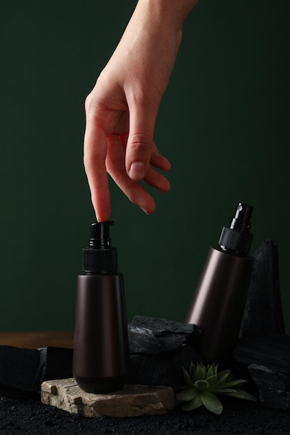 A bottle with natural charcoal cosmetics on a green background