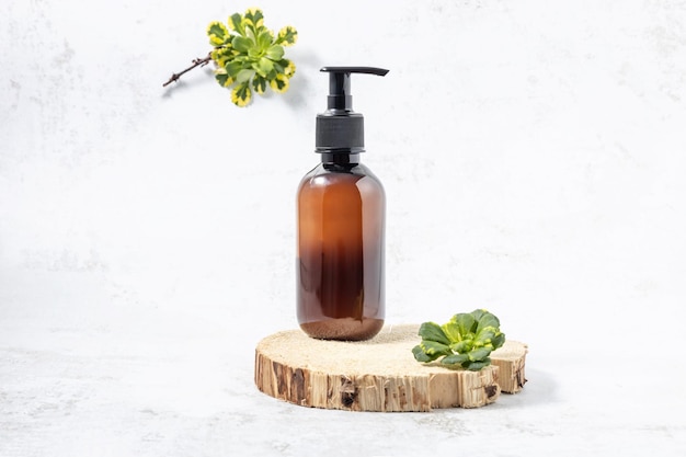 Bottle with a pump on a wooden board and green leaves of succulents