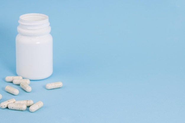 Bottle with scattered pills on blue background with copy space