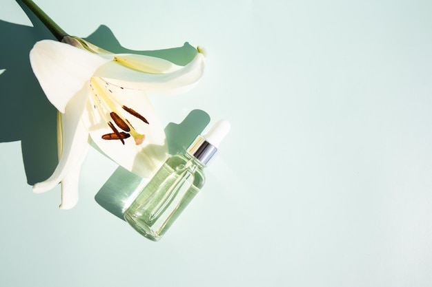 Bottle with a serum for the care of the face on a pastel background with a white lily the concept of natural cosmetics top view space for text