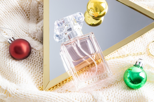 A bottle of women's perfume is reflected in a mirror with Christmas balls knitted beige background Gift conceptfragrance presentation