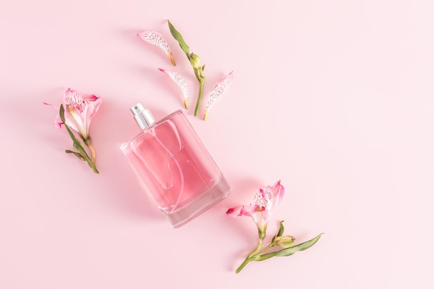 A bottle of women's perfume or toilet water on a pink background among the buds of astromeria product presentation a copy of the space top view