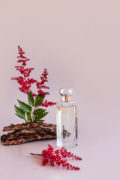 A bottle of women's perfume or toilet water on a pink background with flowers and bark of a tree presentation of the aroma of a natural smell