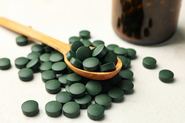 Bottle and wooden spoon with spirulina pills on white textured background